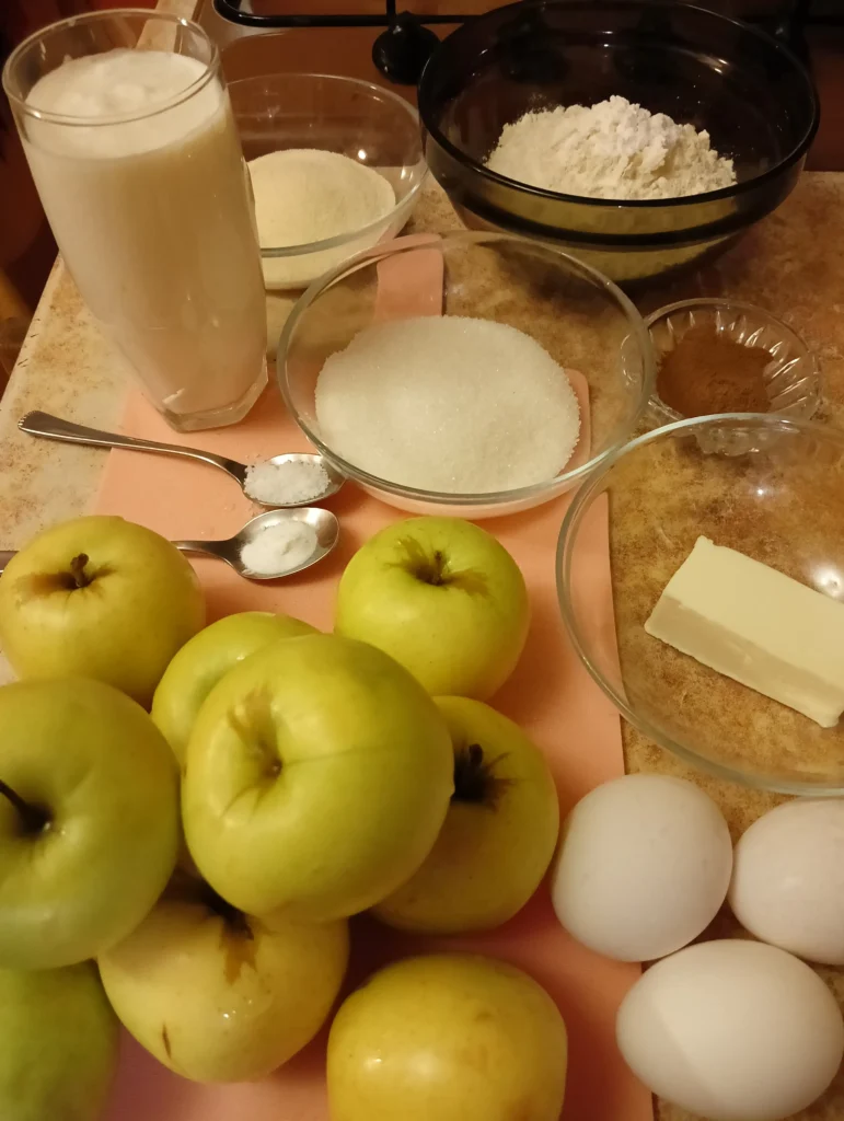 Ingredients for making an apple pie, including apples, flour, sugar, butter, eggs, and cinnamon.