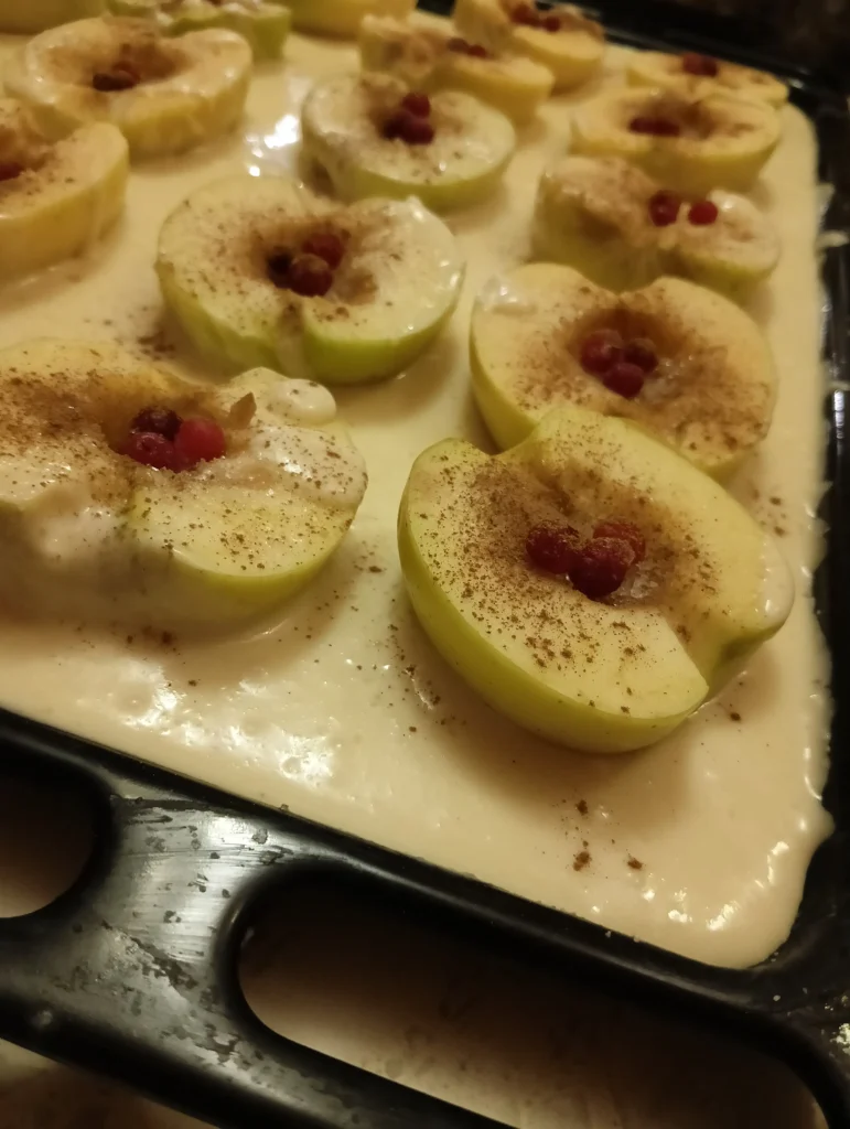 Sliced green apples with cinnamon and berries arranged on a baking tray, ready for the oven.