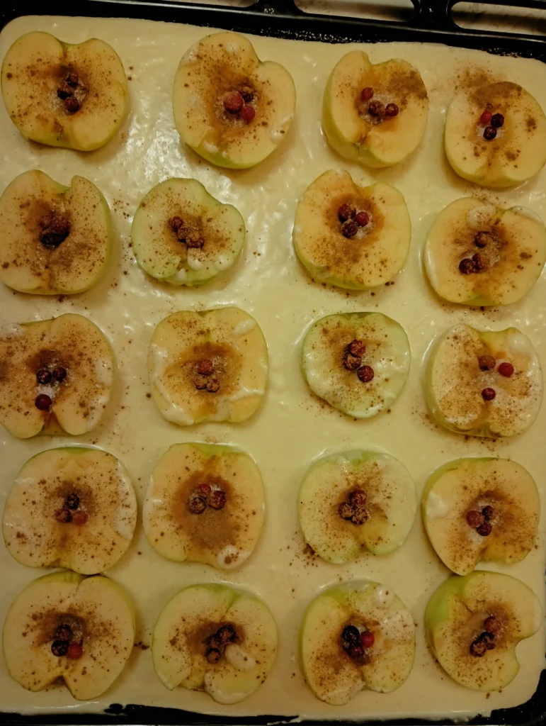 A baking tray filled with sliced apples, topped with cinnamon and berries, ready for the oven.