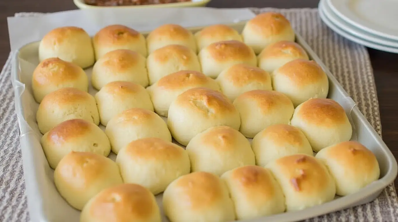 Freshly baked golden-brown no-yeast dinner rolls in a baking tray on a textured placemat