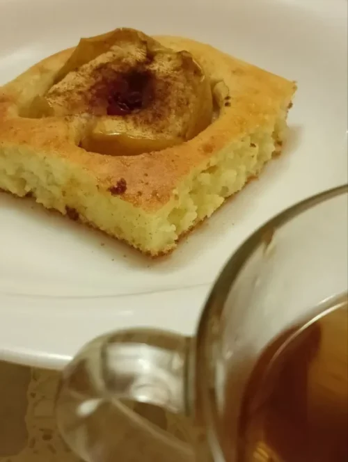 A close-up shot of a slice of baked apple dessert with a cup of tea on the side